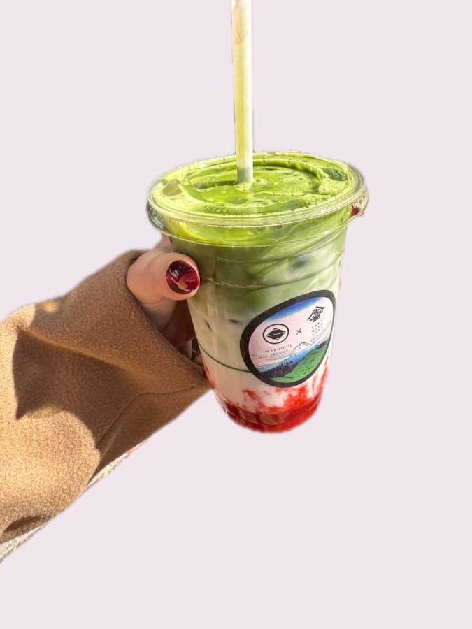 A strawberry matcha latte held up on a sunny walk